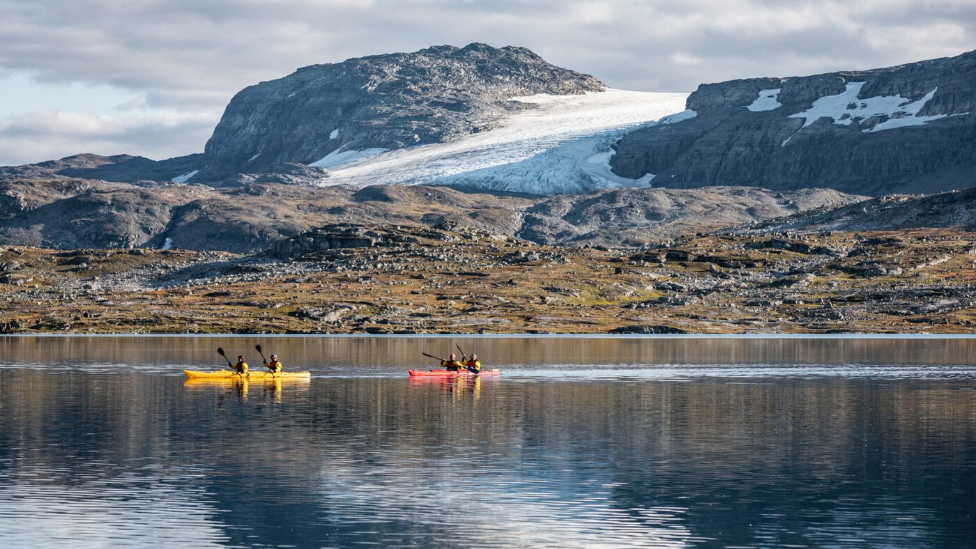 Colourful kayaks on still water beneath a rugged mountain landscape