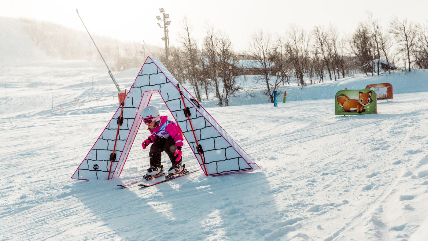 A child skiing through a colourful play feature in a snowy beginner area