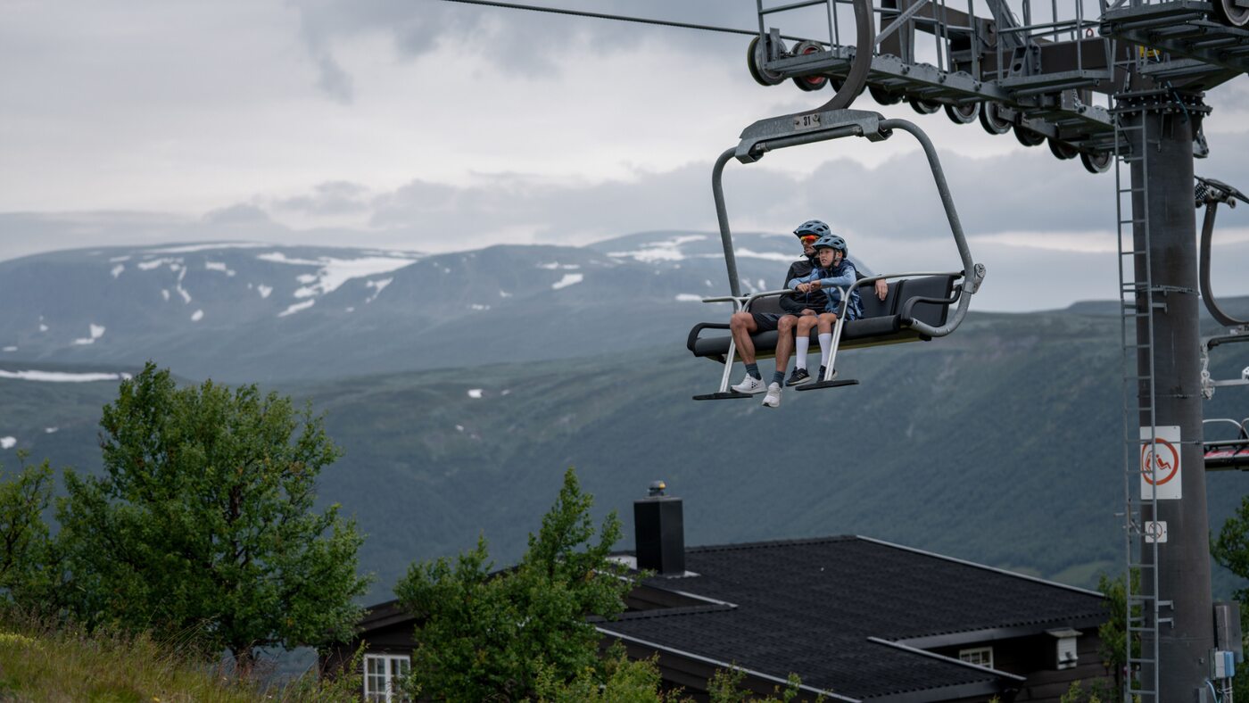 Two passengers riding a chairlift above a green mountain landscape